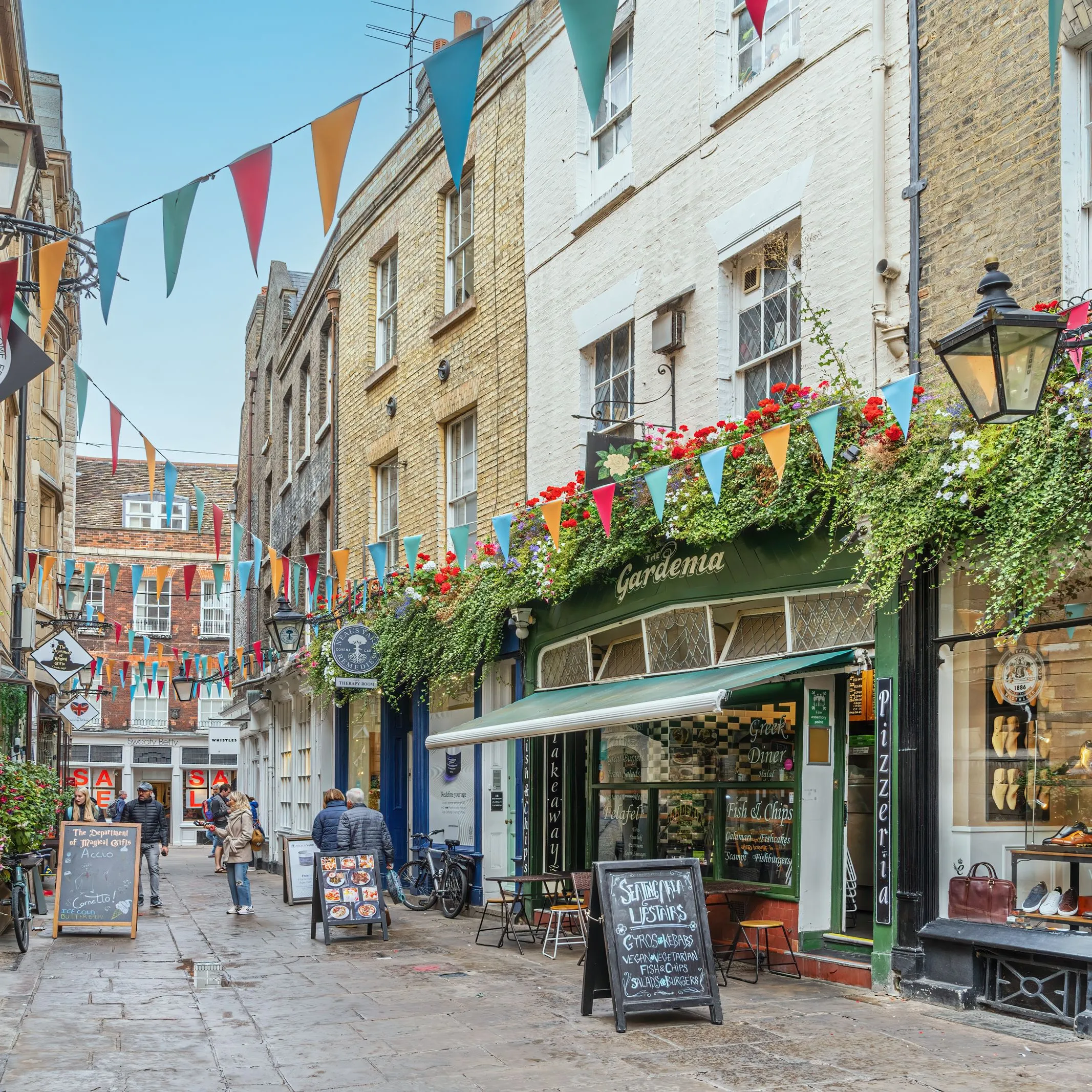 People browsing a flower-filled lane of cafés and boutiques while shopping in Cambridge.