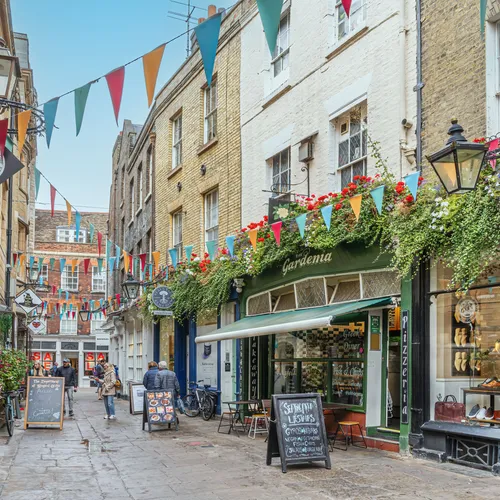 People browsing a flower-filled lane of cafés and boutiques while shopping in Cambridge.