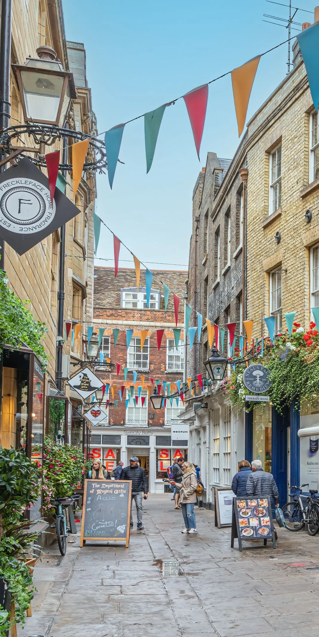 People browsing a flower-filled lane of cafés and boutiques while shopping in Cambridge.