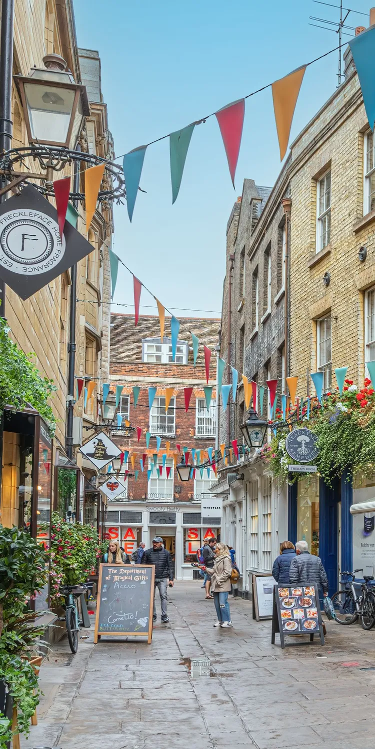 People browsing a flower-filled lane of cafés and boutiques while shopping in Cambridge.