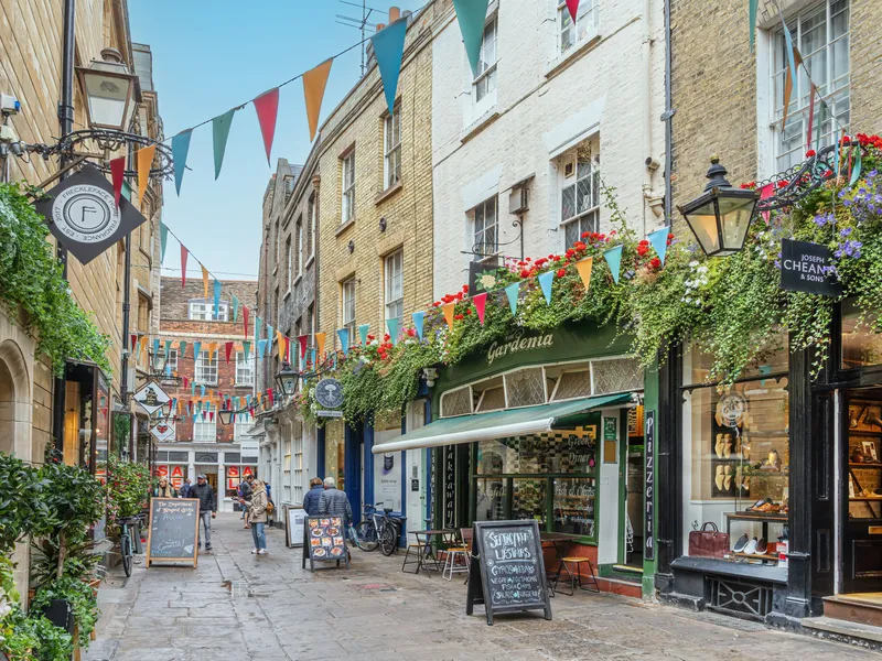 People browsing a flower-filled lane of cafés and boutiques while shopping in Cambridge.