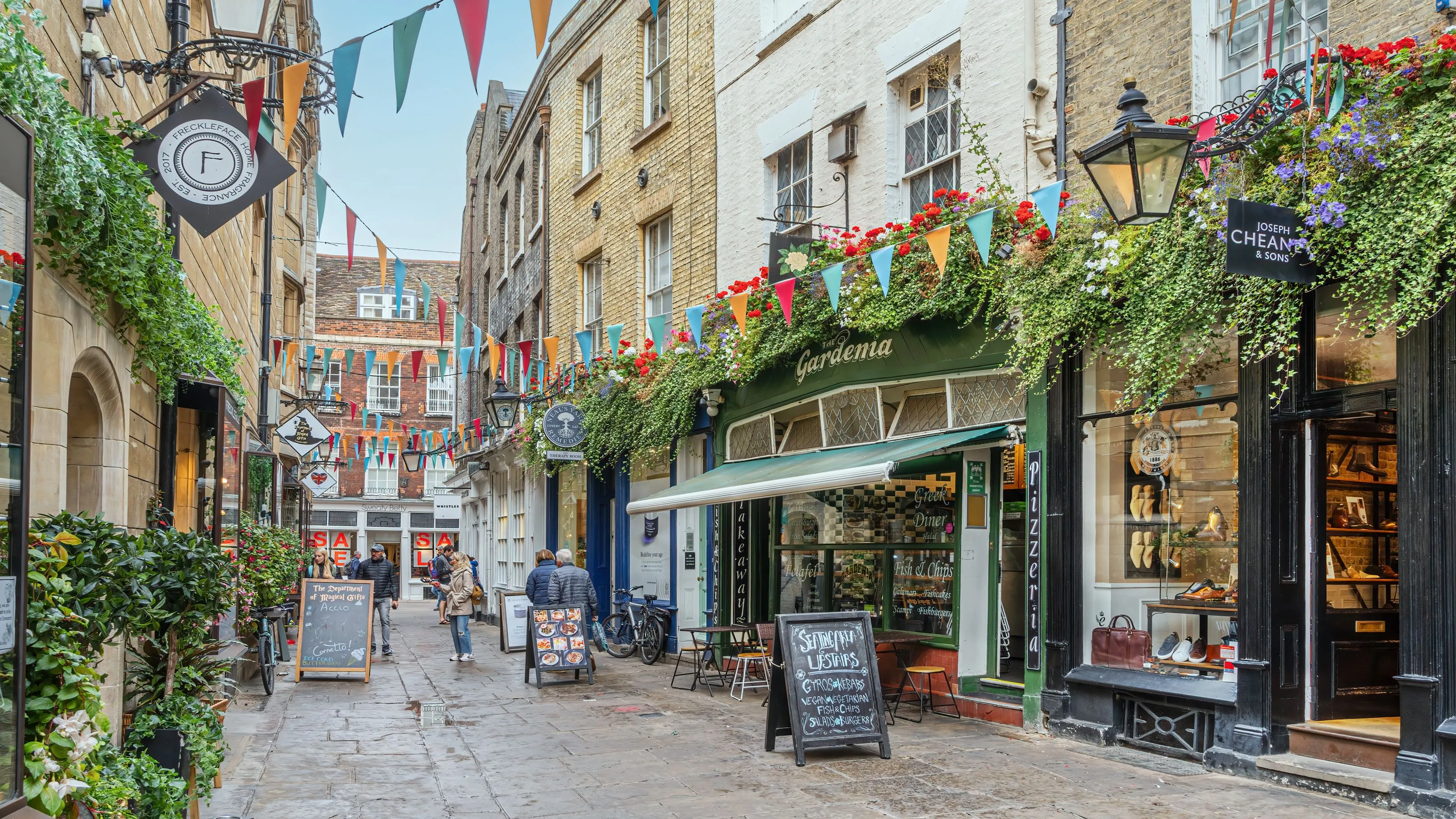 People browsing a flower-filled lane of cafés and boutiques while shopping in Cambridge.