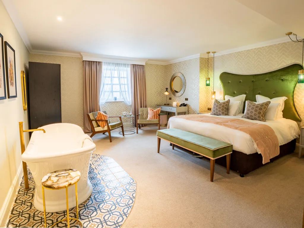 Spacious boutique hotel bedroom with a freestanding bath, green upholstered headboard and elegant seating area