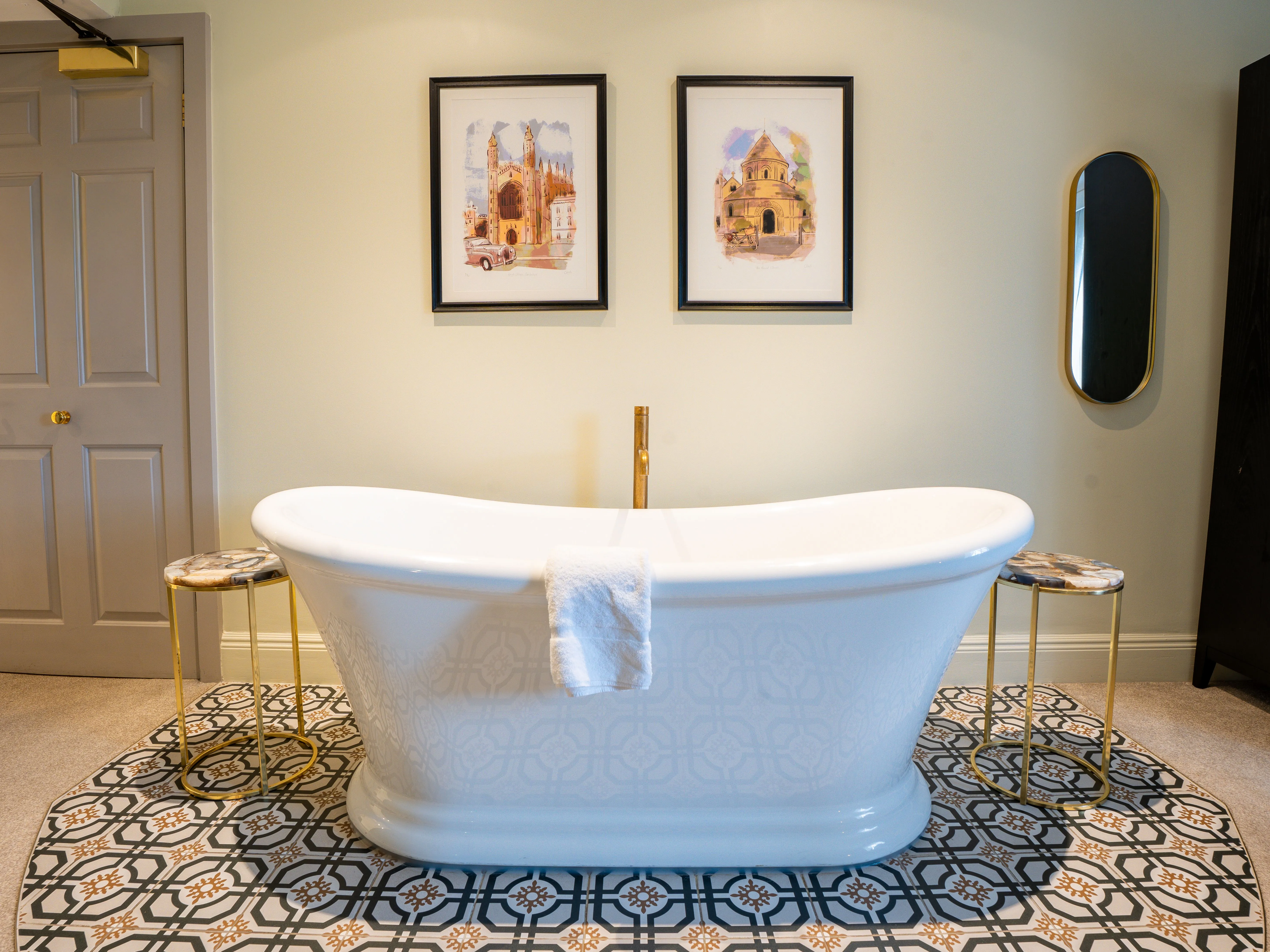 Freestanding white bath in an elegant bathroom with patterned floor tiles, framed artwork and a wall mirror