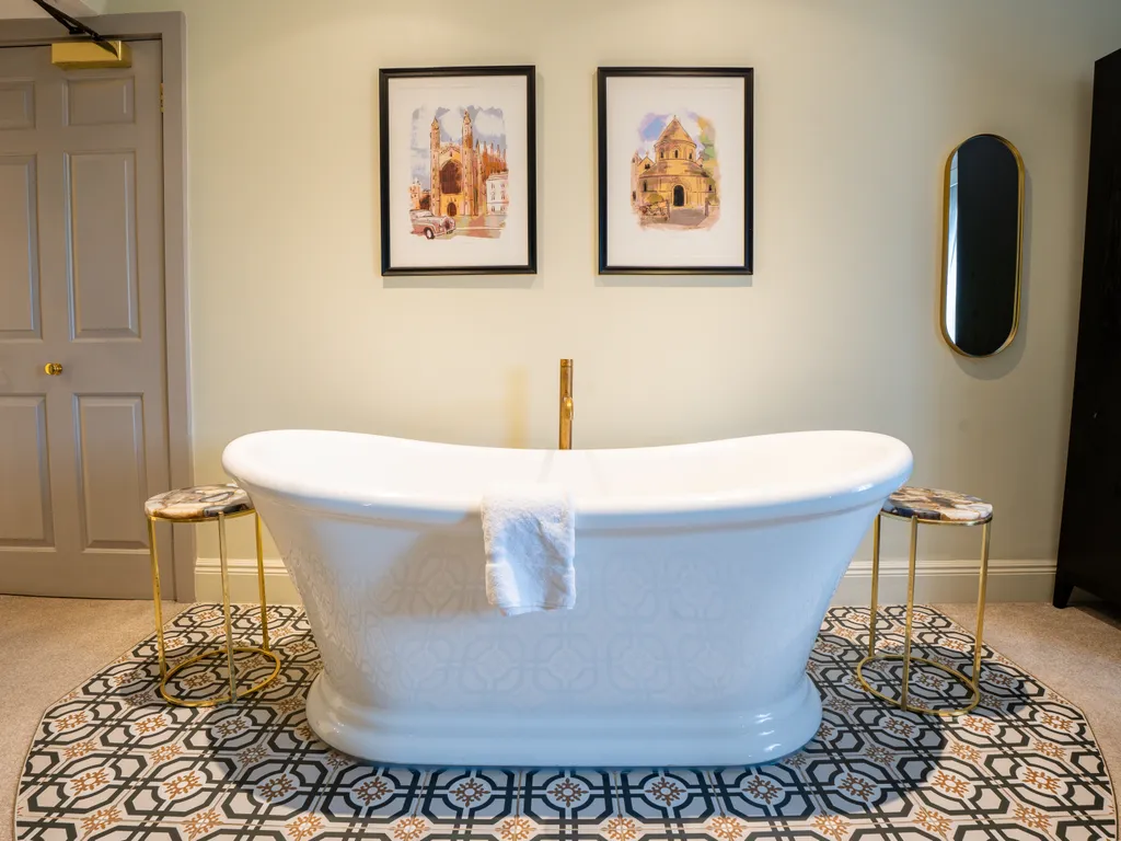 Freestanding white bath in an elegant bathroom with patterned floor tiles, framed artwork and a wall mirror