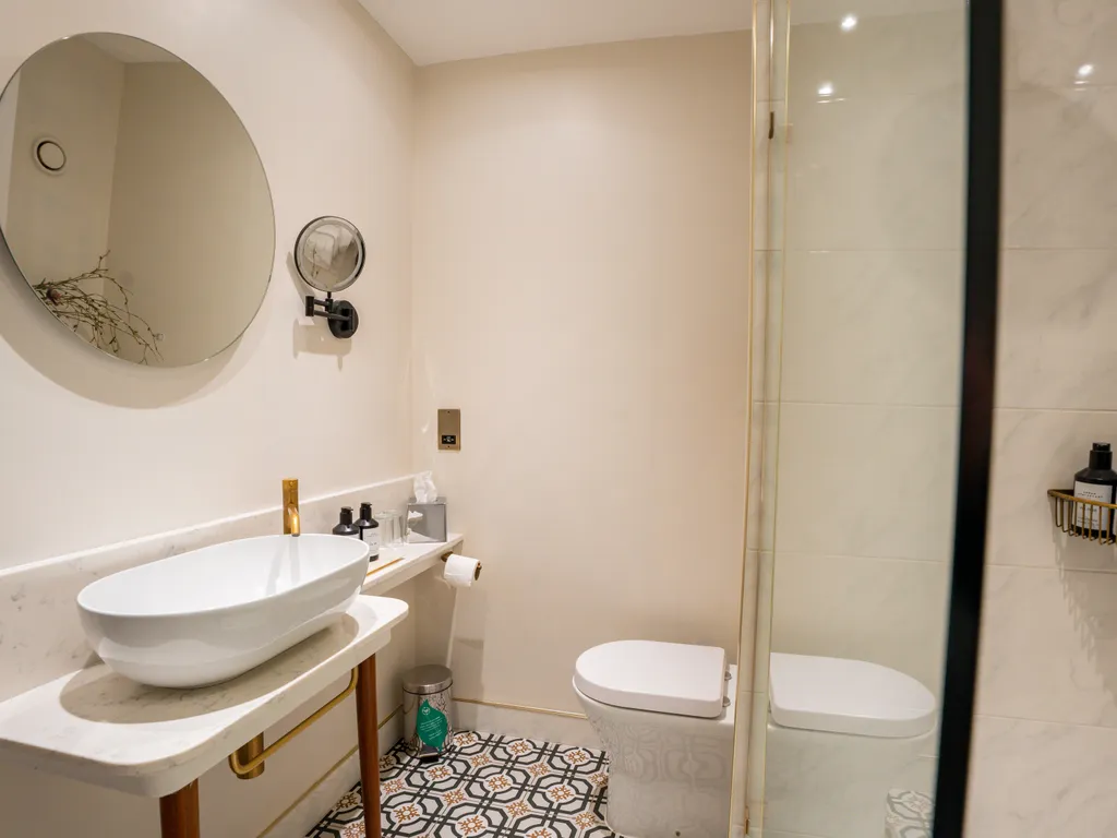 Modern bathroom with a round mirror, marble-style sink, toilet and glass shower enclosure