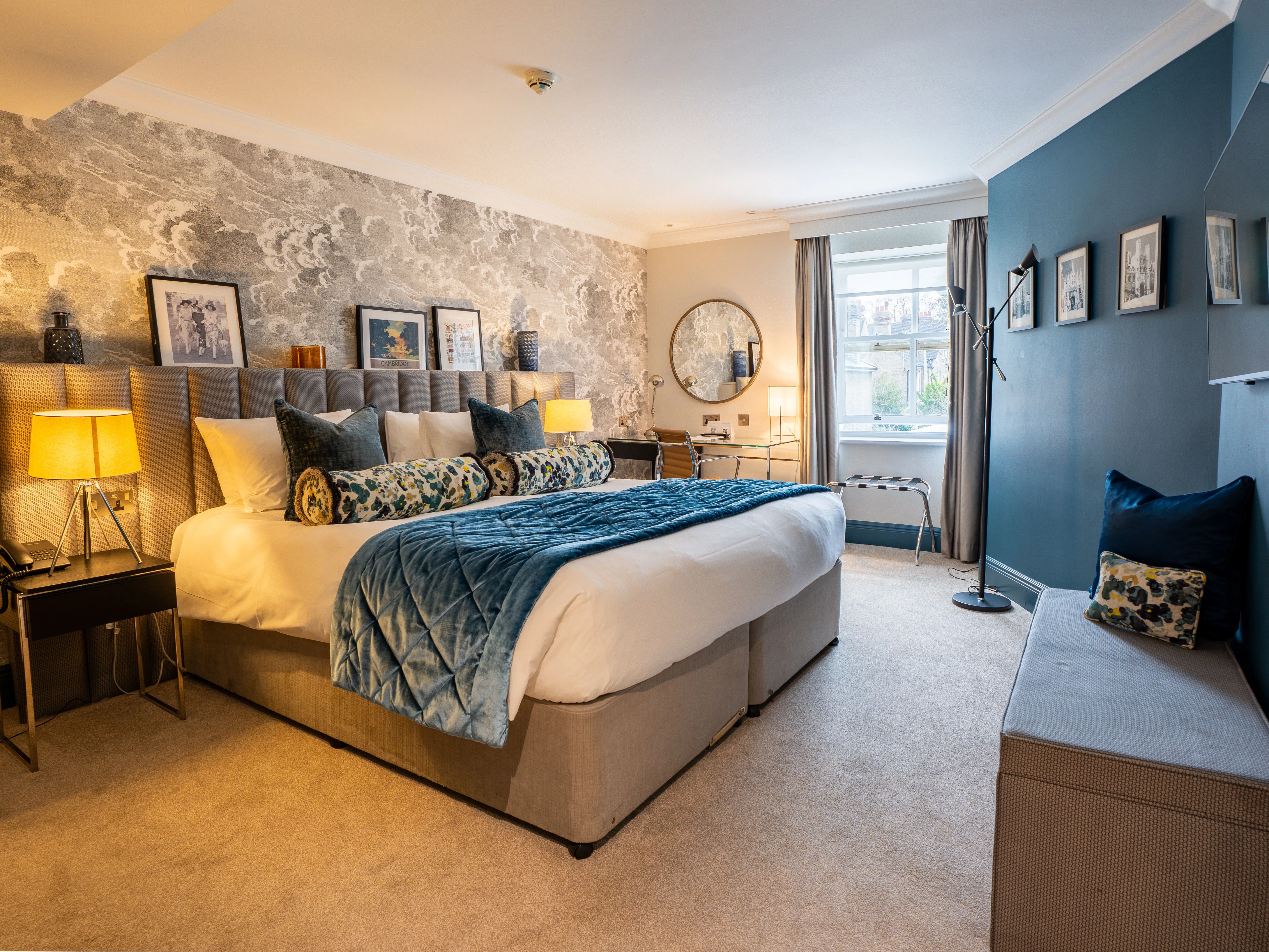 Elegant hotel bedroom with blue accents, patterned wallpaper, a king-size bed, desk and wall-mounted television