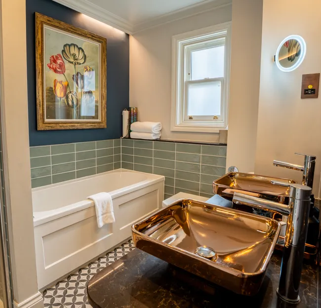 Stylish bathroom with walk-in shower, bath, teal wall tiles and metallic vessel sinks