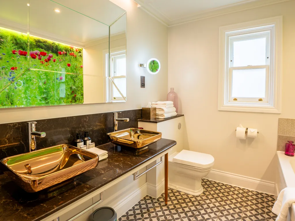 Elegant bathroom with black marble vanity, twin metallic basins, patterned floor tiles and a large illuminated mirror