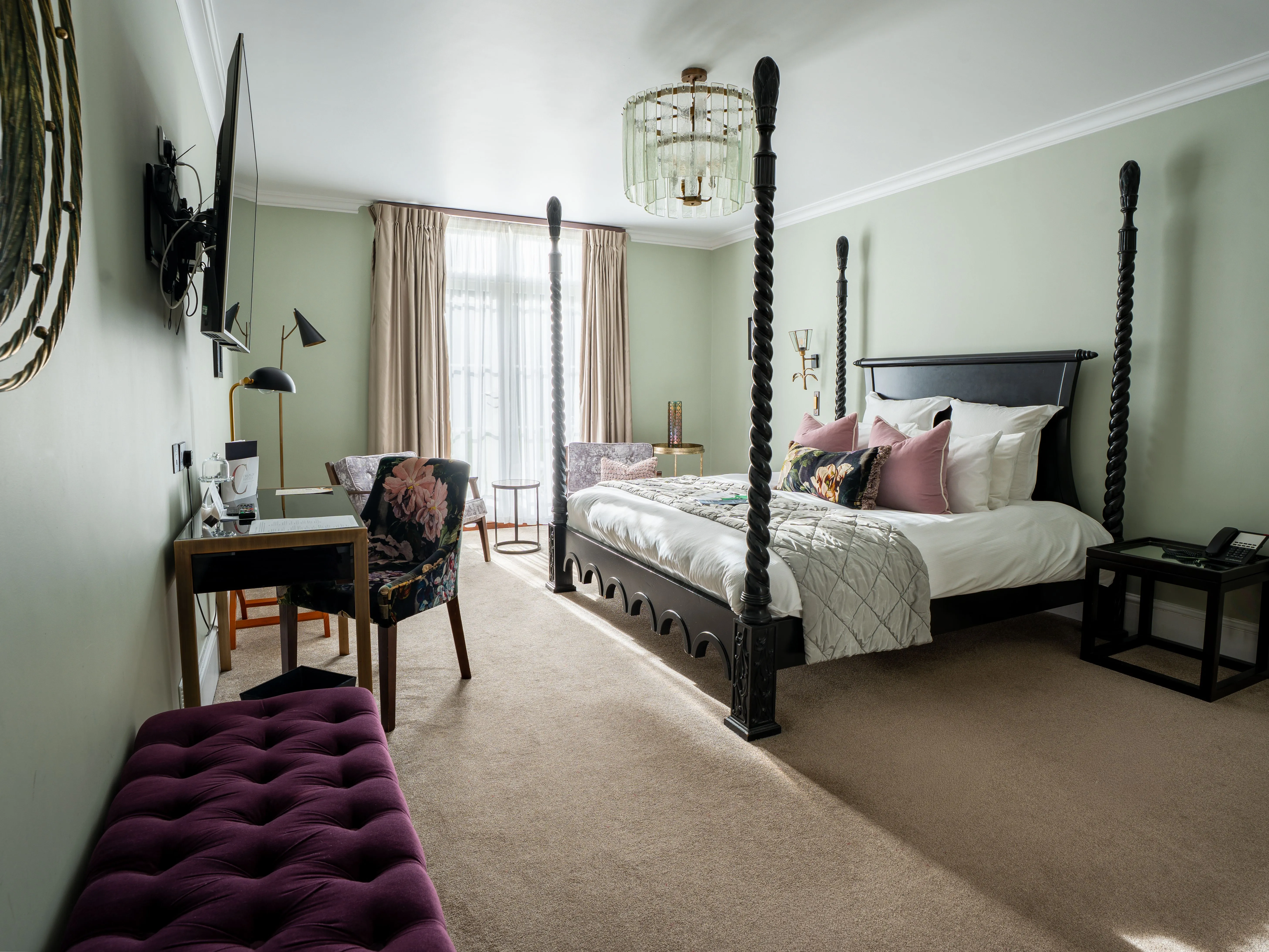 Elegant bedroom with a dark four-poster bed, sage green walls, a writing desk and soft natural light from tall windows