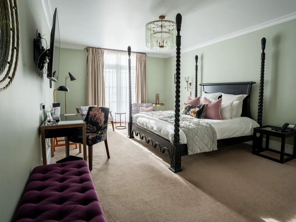 Elegant bedroom with a dark four-poster bed, sage green walls, a writing desk and soft natural light from tall windows