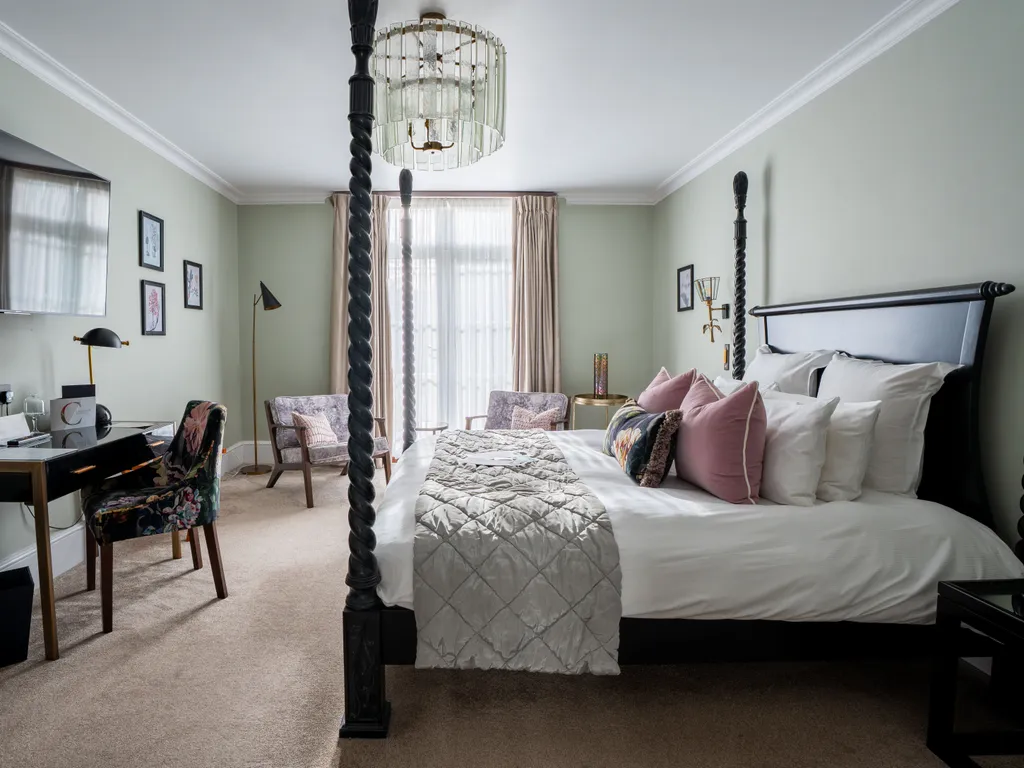 Elegant bedroom with a black four-poster bed, desk, wall-mounted television and seating area by tall curtained windows.