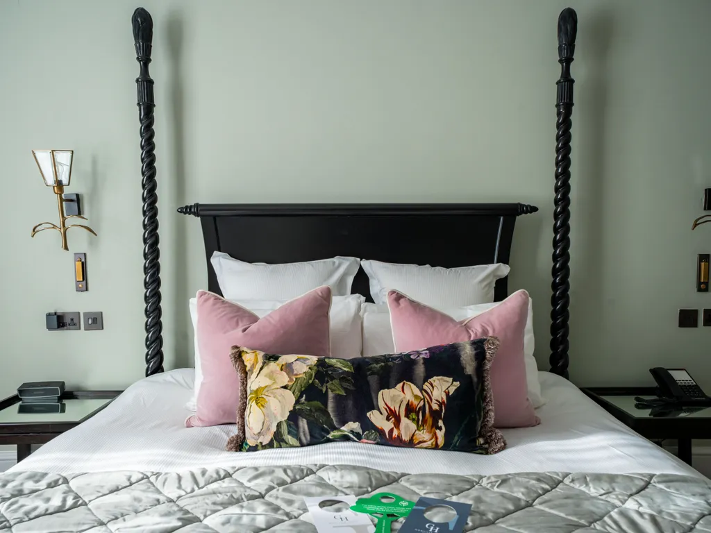 Elegant four-poster bed with twisted black posts, pink cushions and a floral bolster in a stylish bedroom.