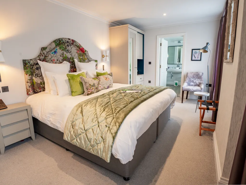 Elegant bedroom with a large bed, floral upholstered headboard, bedside tables and an en-suite bathroom