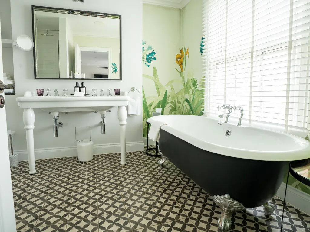 Elegant bathroom with a black clawfoot bath, pedestal sink, large mirror, patterned floor tiles and botanical wall mural.