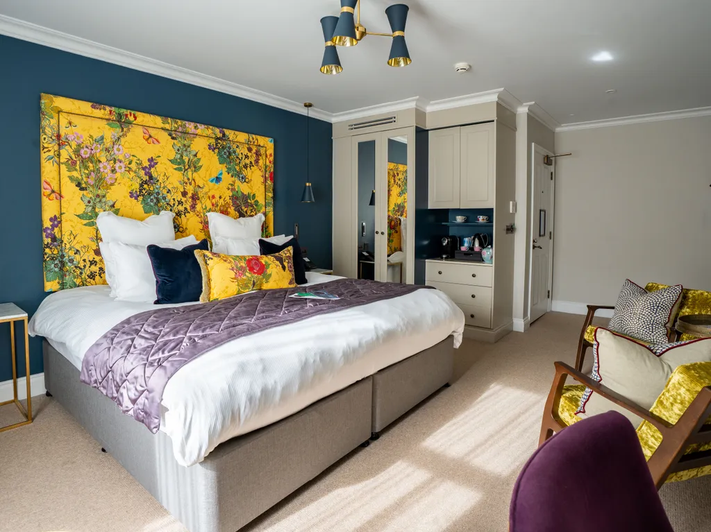Stylish boutique bedroom with a floral yellow headboard, deep blue feature wall, king-size bed and elegant seating area
