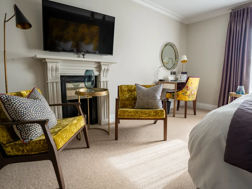 Elegant bedroom seating area with mustard velvet armchairs, a fireplace, wall-mounted television and purple curtains