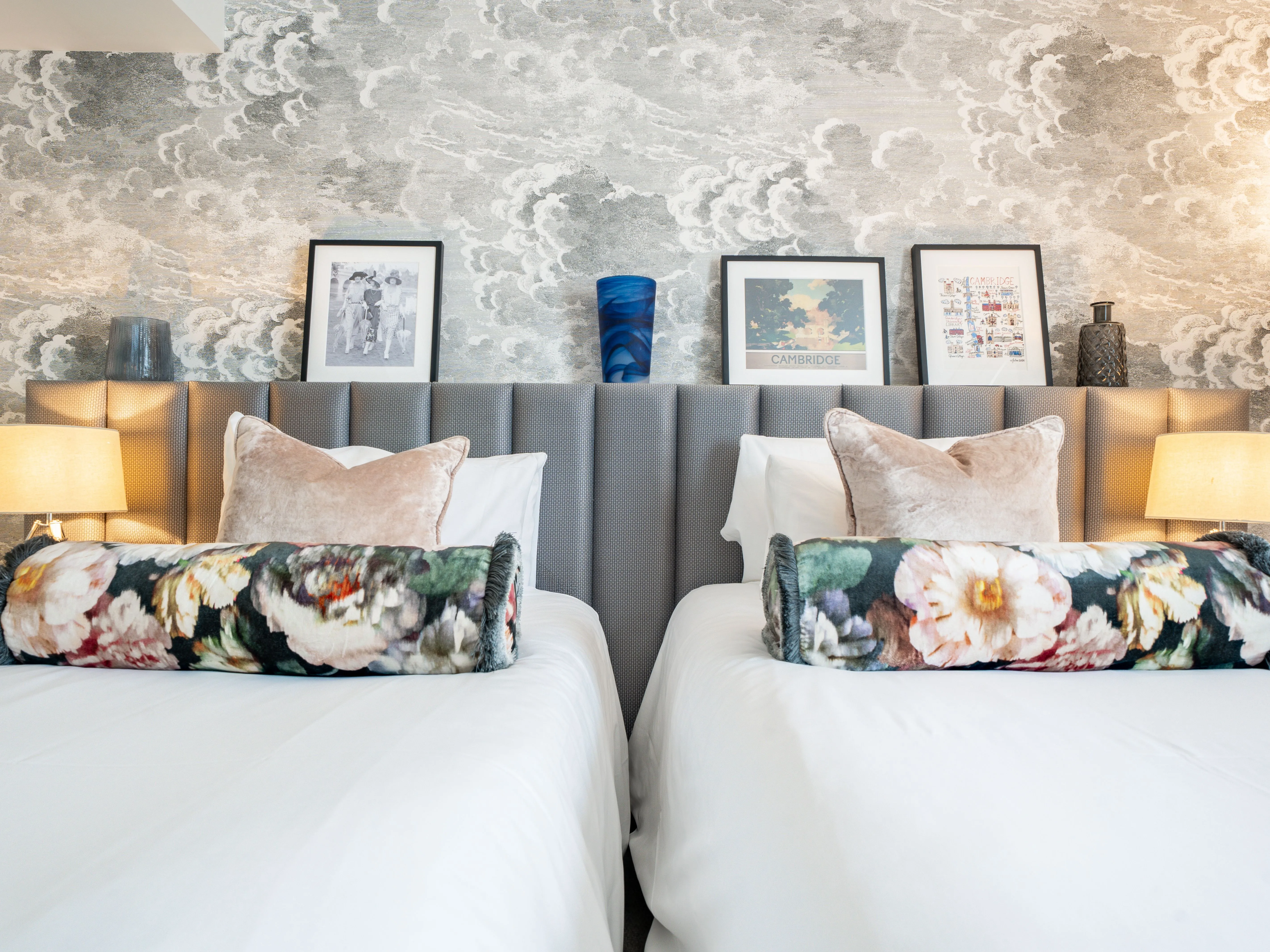 Stylish twin bedroom with upholstered headboard, floral cushions and cloud-pattern wallpaper