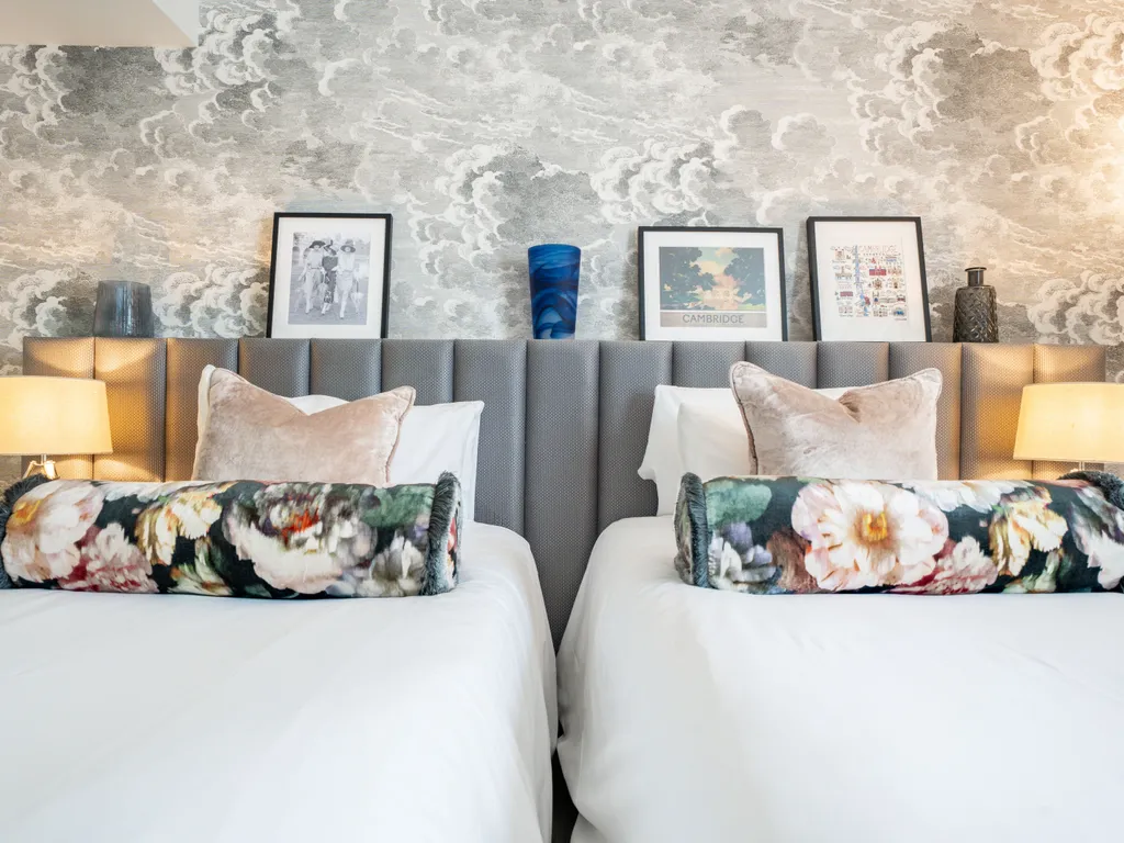 Stylish twin bedroom with upholstered headboard, floral cushions and cloud-pattern wallpaper