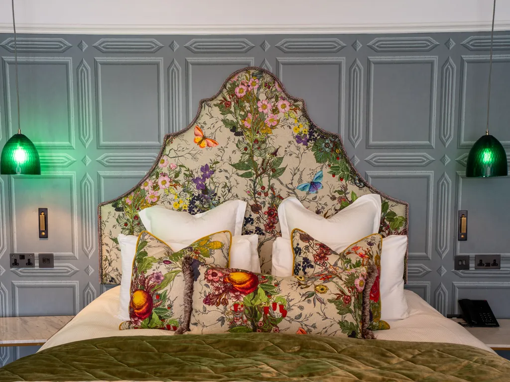 Elegant bedroom with a floral upholstered headboard, matching cushions, grey panelled walls and green pendant lights
