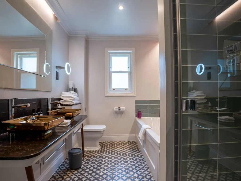 Stylish modern bathroom with twin basin vanity, patterned floor tiles, bath and glass shower enclosure