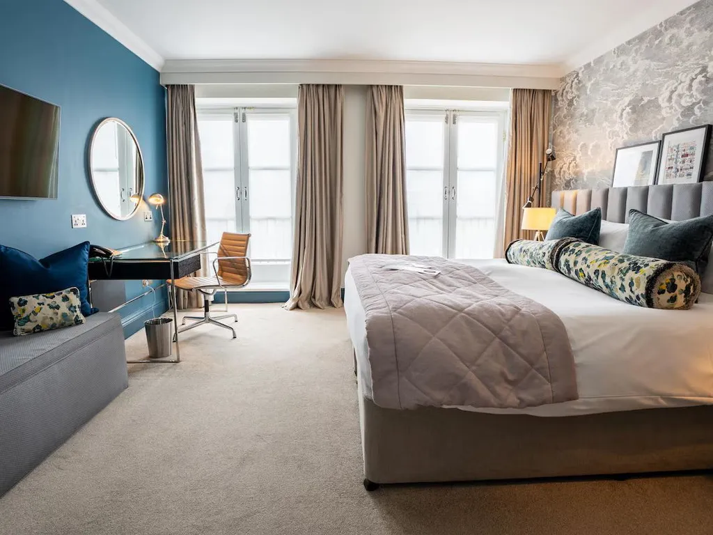 Stylish hotel bedroom with a large bed, desk, wall-mounted television and tall windows with curtains