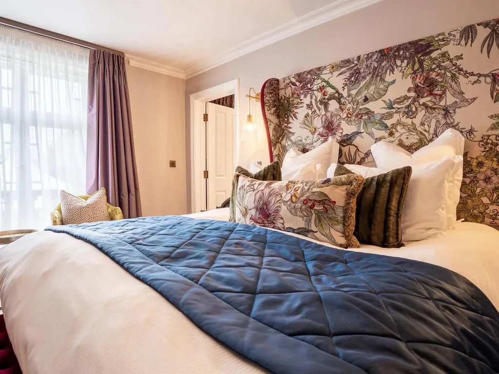 Elegant bedroom with floral upholstered headboard, blue quilted bed runner and soft purple curtains