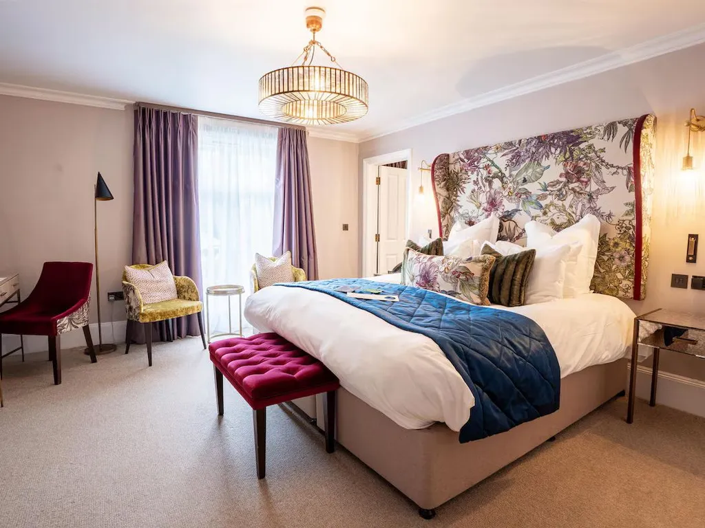 Elegant hotel bedroom with a floral upholstered headboard, king-size bed, purple curtains and colourful seating