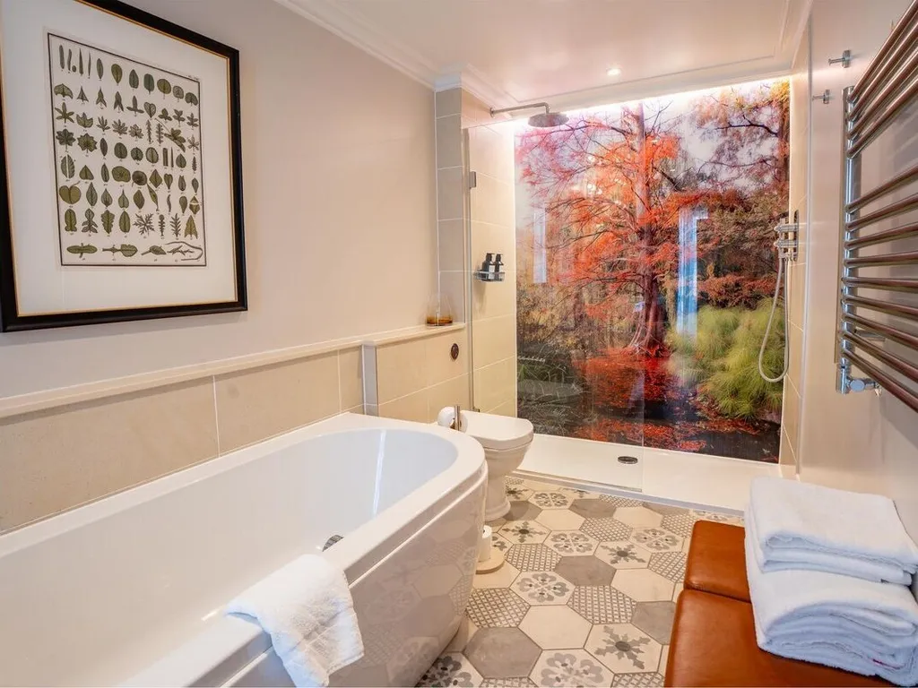Modern bathroom with freestanding bath, patterned floor tiles and a walk-in shower featuring a colourful autumn woodland mural