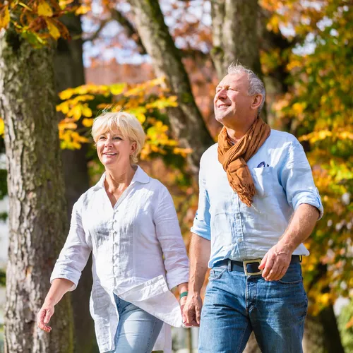 Middle-aged couple walking hand in hand through a park with autumn trees in bright sunshine