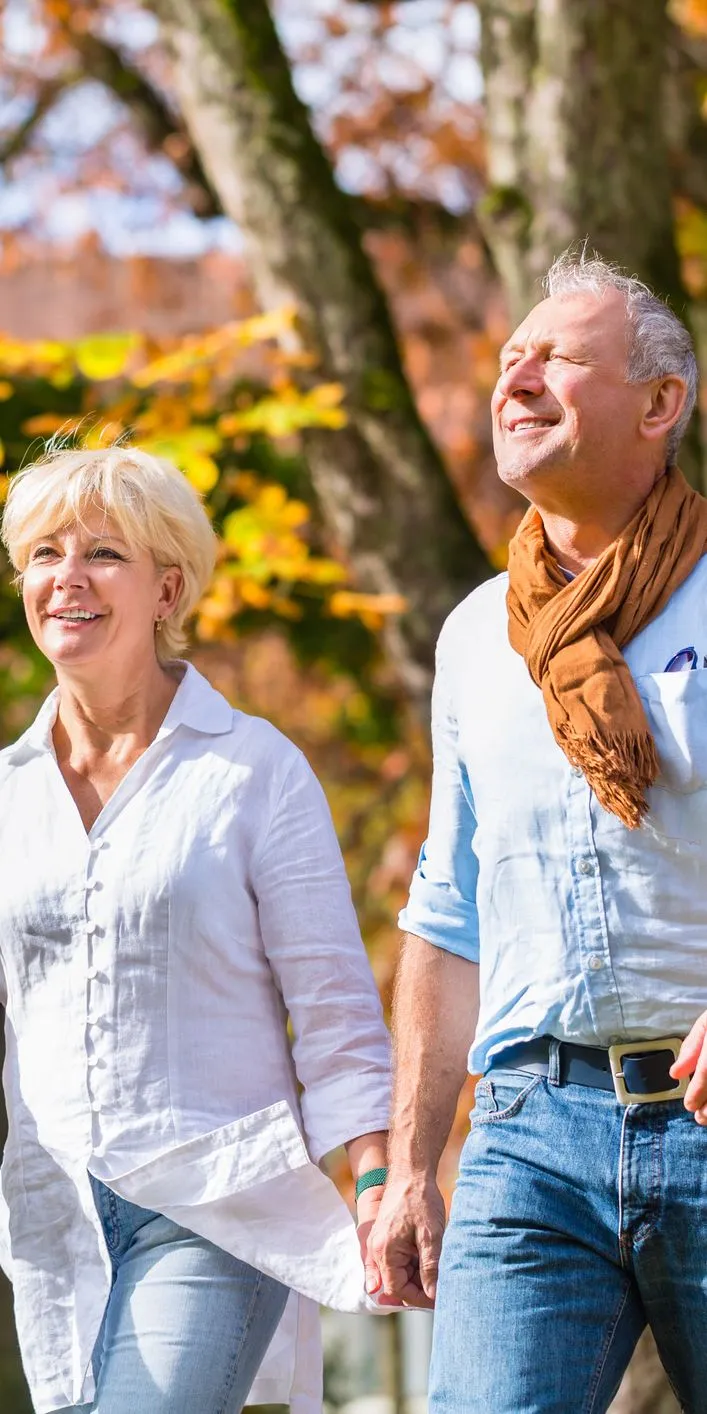 Middle-aged couple walking hand in hand through a park with autumn trees in bright sunshine