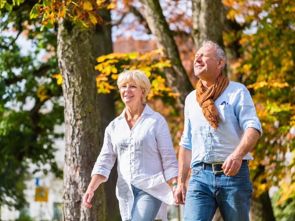 Middle-aged couple walking hand in hand through a park with autumn trees in bright sunshine