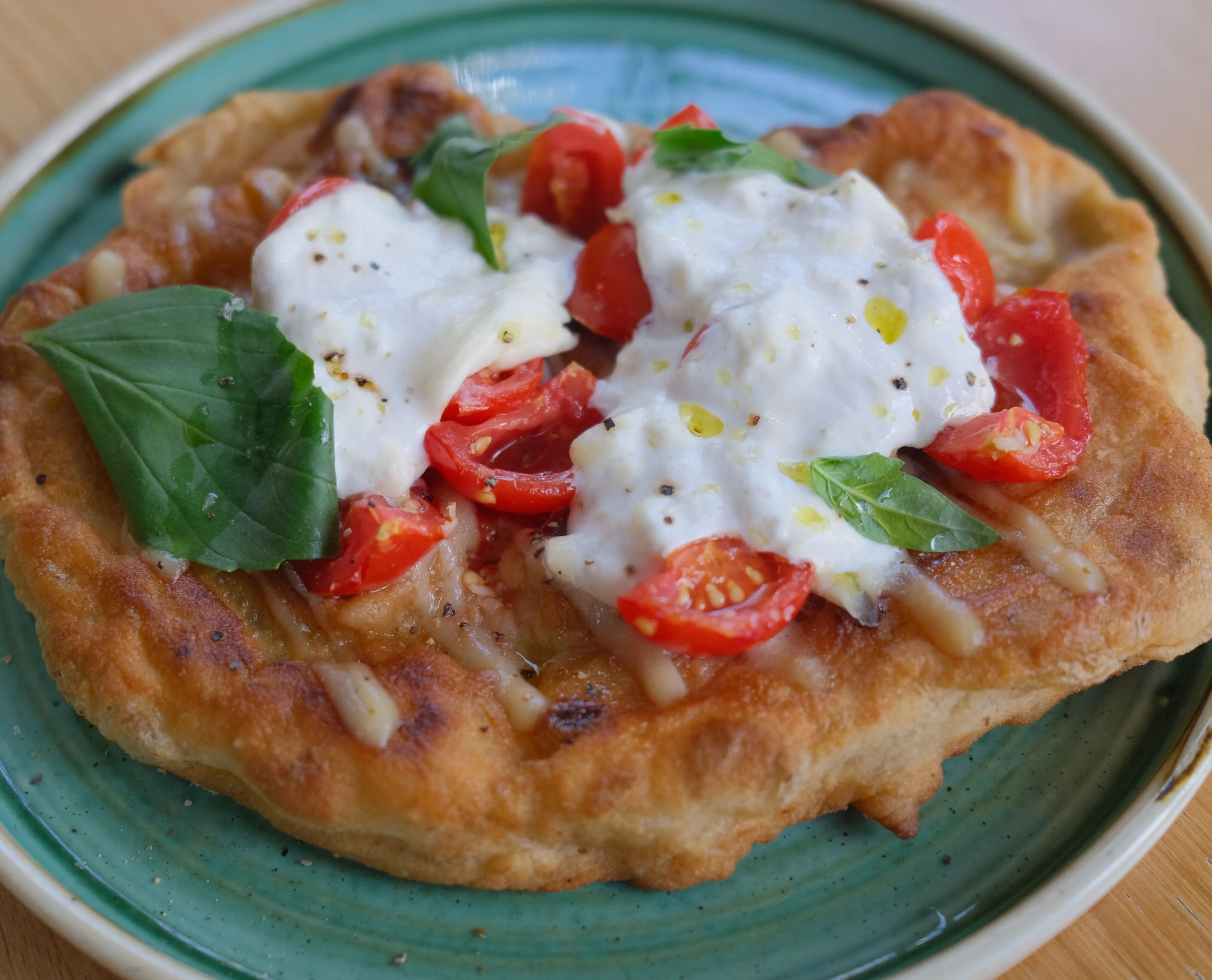 Fried dough bread topped with burrata, cherry tomatoes and fresh basil on a green plate