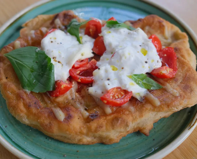 Fried dough bread topped with burrata, cherry tomatoes and fresh basil on a green plate