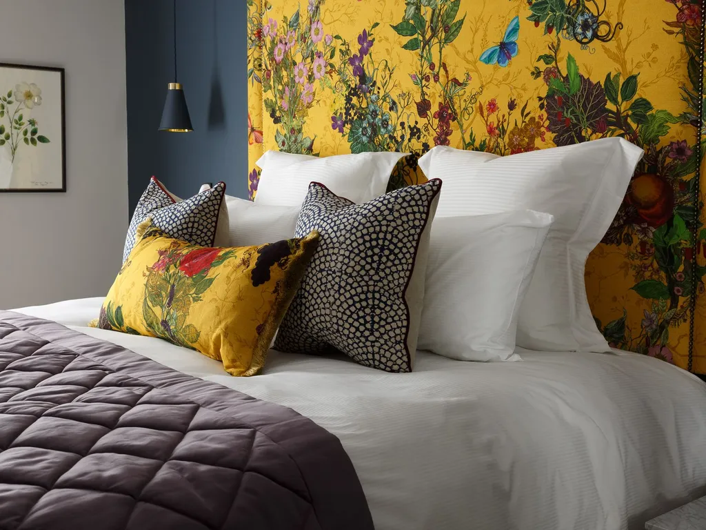 Stylish bedroom with a mustard yellow floral headboard, white bedding and patterned cushions