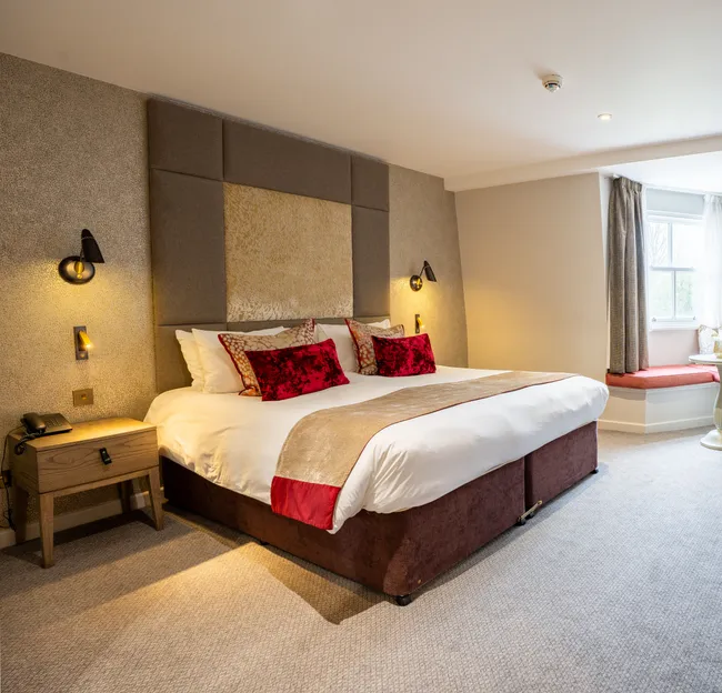 Spacious contemporary hotel bedroom with a king-size bed, desk, red armchair and window seating area