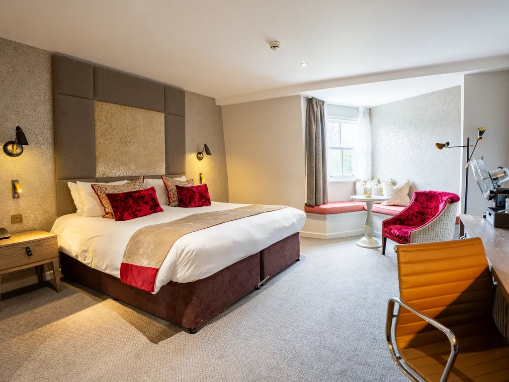 Spacious contemporary hotel bedroom with a king-size bed, desk, red armchair and window seating area