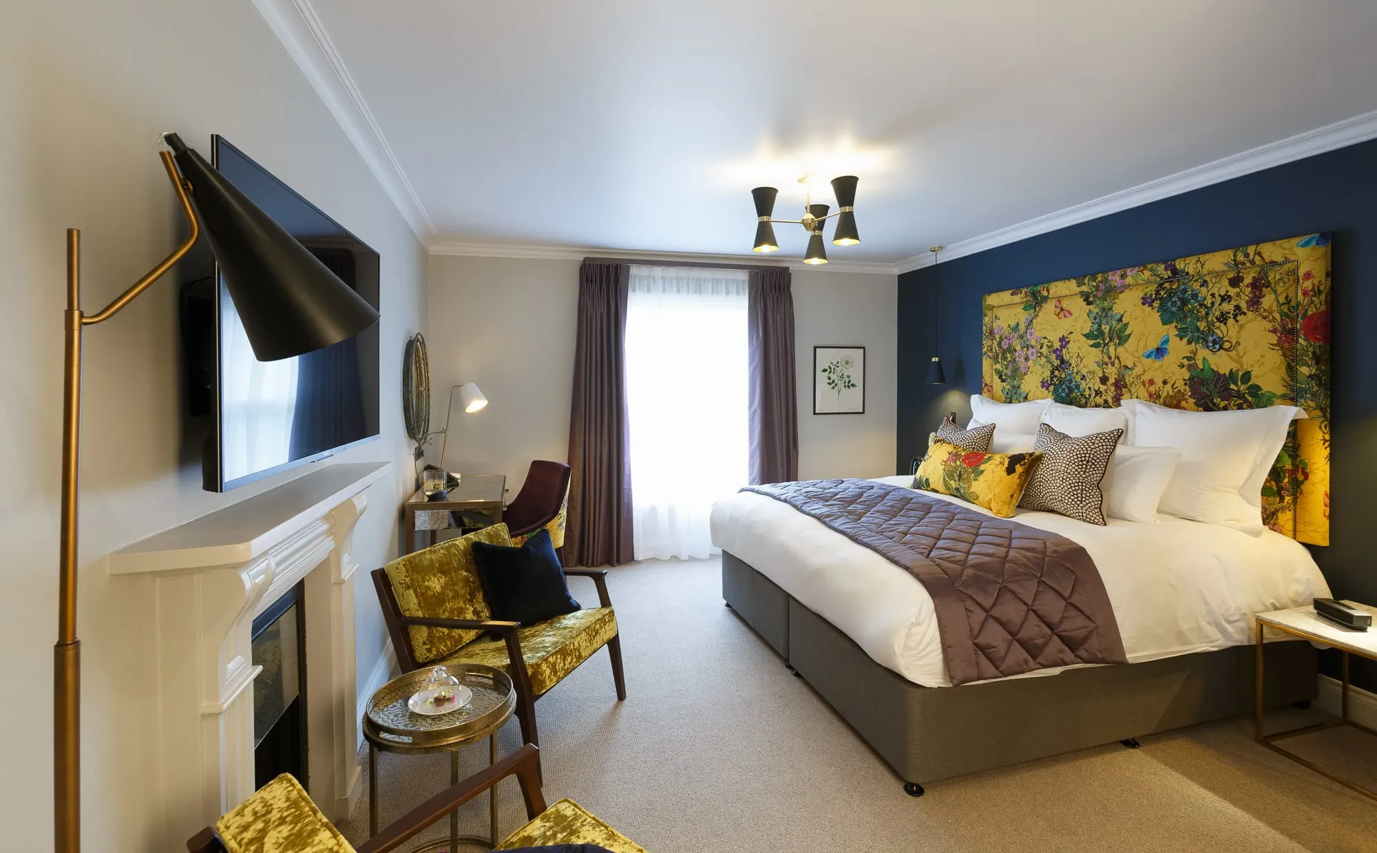 The Rosa feature room at Gonville Hotel in Cambridge, with bold floral décor, plush bedding, velvet chairs, and a cosy, modern design.
