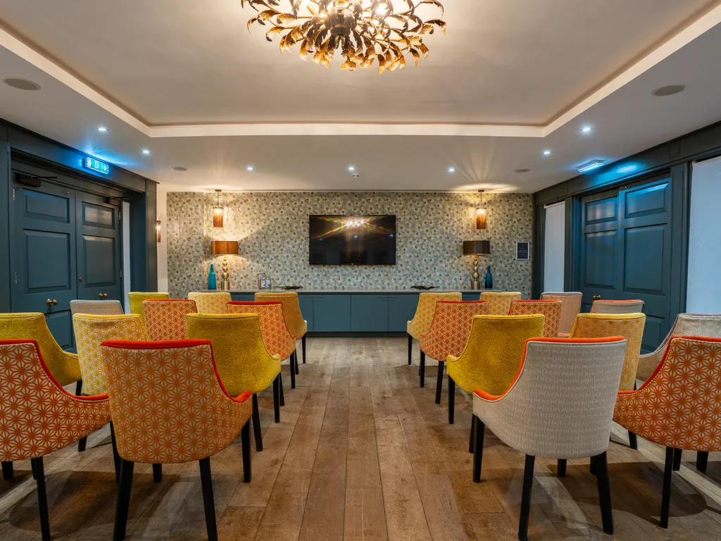 Stylish meeting or presentation room with patterned upholstered chairs, dark blue panelling, wooden flooring and a wall-mounted television.