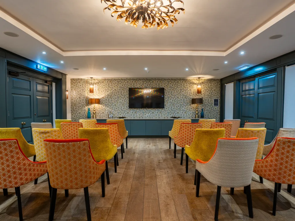 Stylish meeting or presentation room with patterned upholstered chairs, dark blue panelling, wooden flooring and a wall-mounted television.