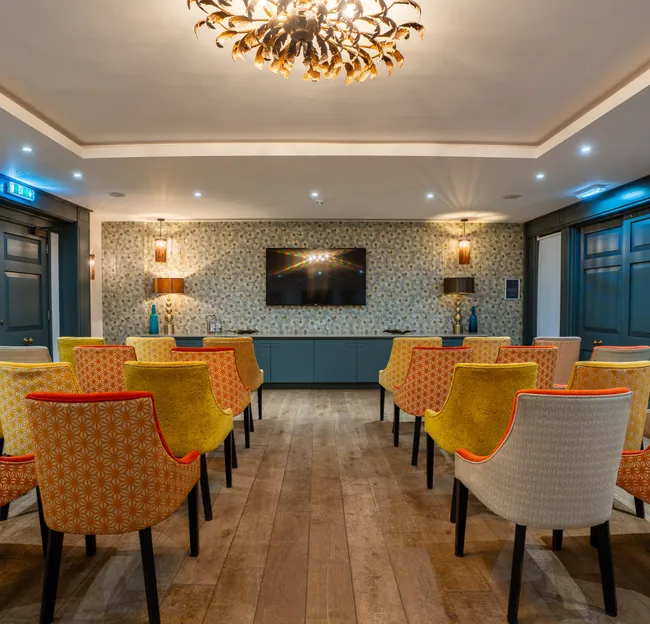 Stylish meeting or presentation room with patterned upholstered chairs, dark blue panelling, wooden flooring and a wall-mounted television.