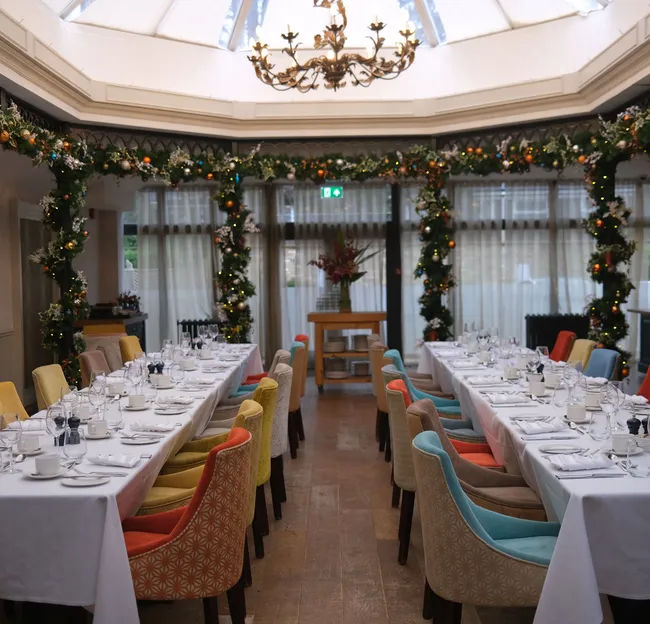 Festively decorated atrium dining room with long tables set for a formal meal beneath a chandelier and skylight.
