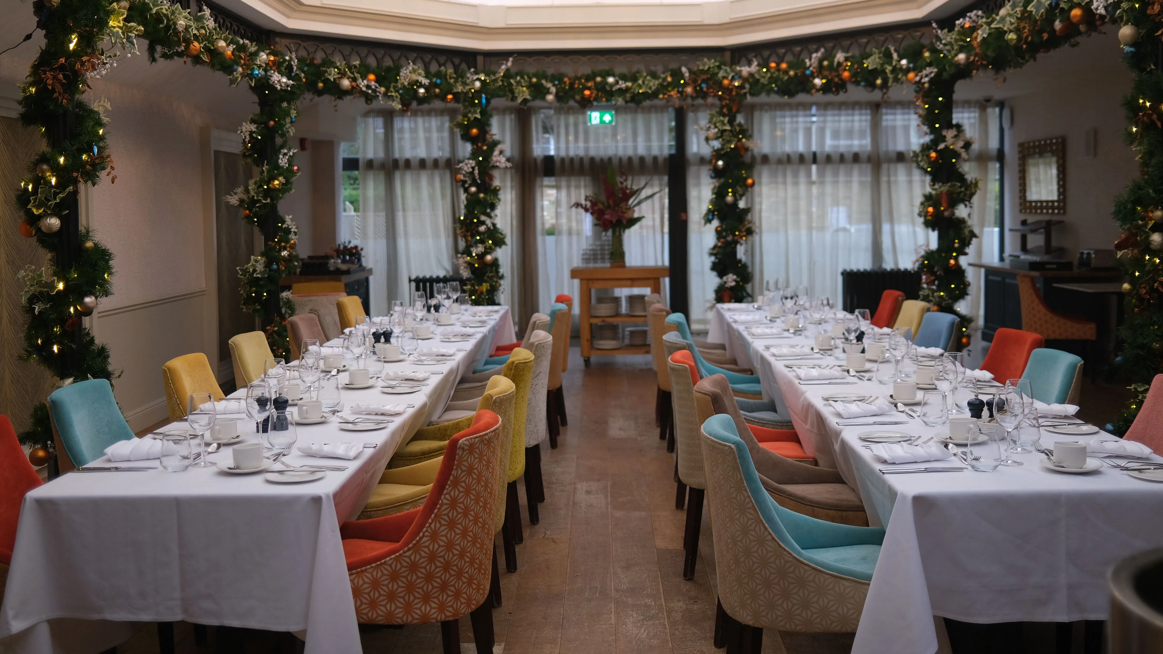 Festively decorated atrium dining room with long tables set for a formal meal beneath a chandelier and skylight.
