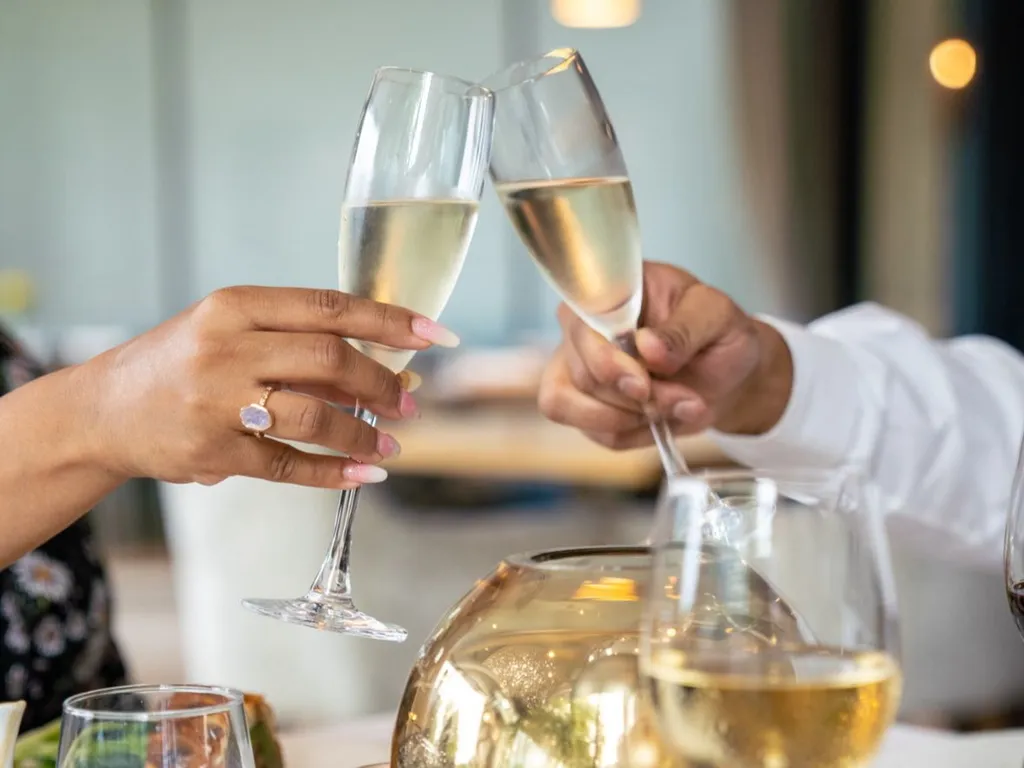Two people clinking champagne flutes over a warmly lit restaurant table