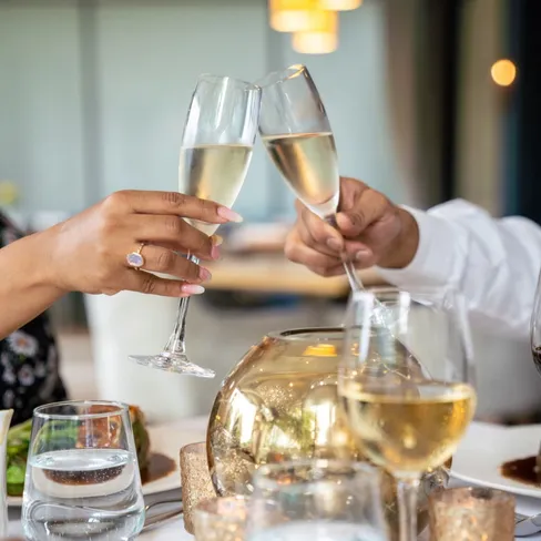 Two people clinking champagne flutes over a warmly lit restaurant table