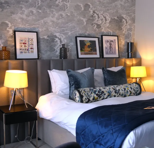 Cosy contemporary bedroom with a neatly made bed, blue quilt, patterned cushions and warm bedside lamps.