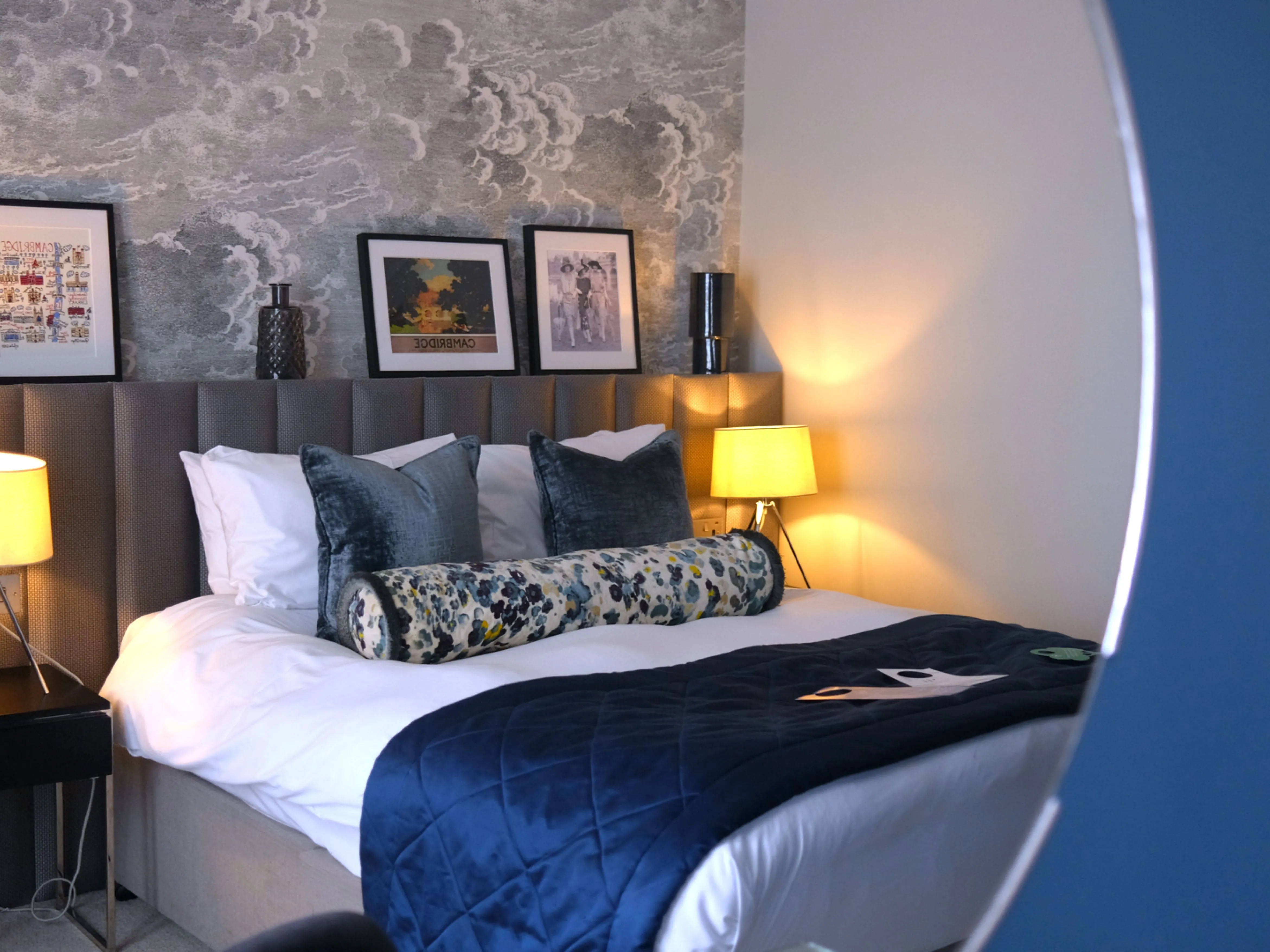 Cosy contemporary bedroom with a neatly made bed, blue quilt, patterned cushions and warm bedside lamps.