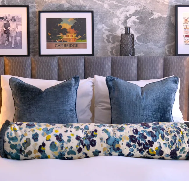 Cosy bedroom with a cushioned headboard, blue velvet cushions, floral bolster and warm bedside lamps.