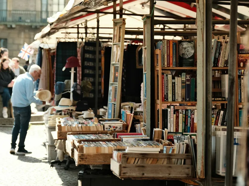 Outdoor book market stall with shelves and crates of second-hand books beneath striped awnings