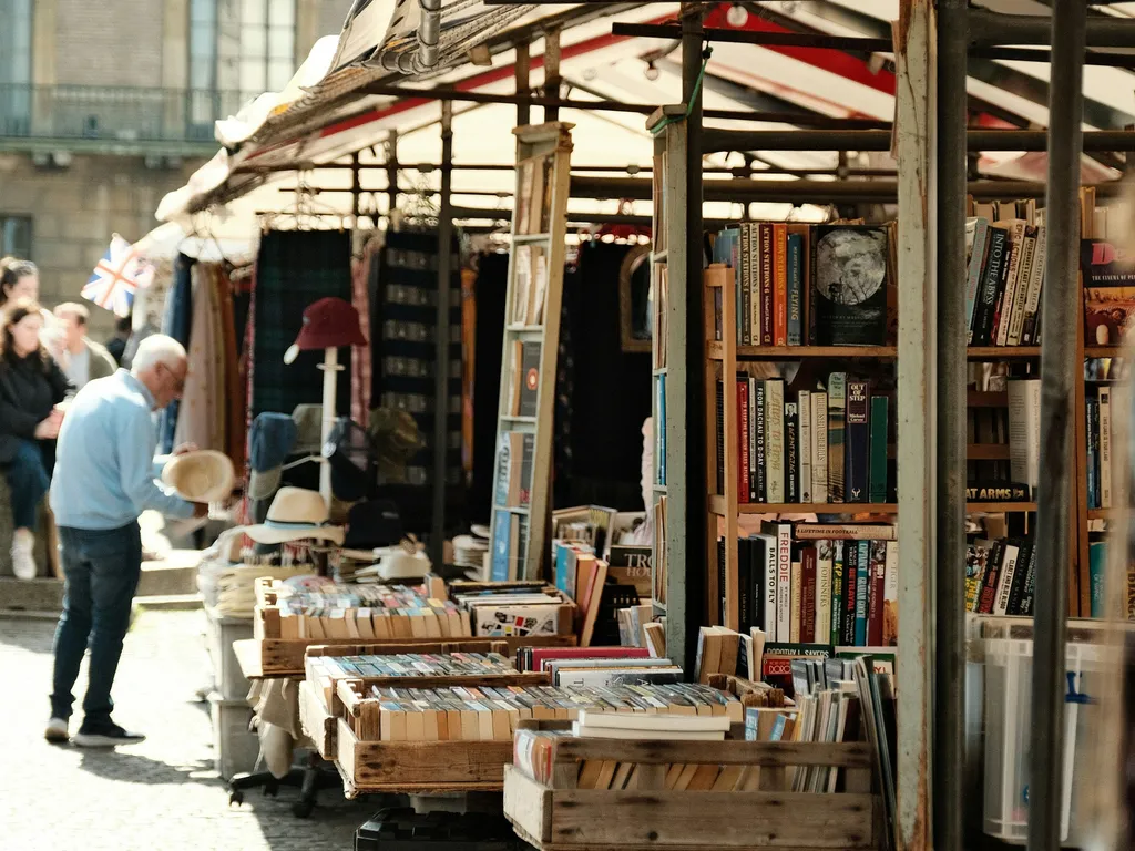 Outdoor book market stall with shelves and crates of second-hand books beneath striped awnings